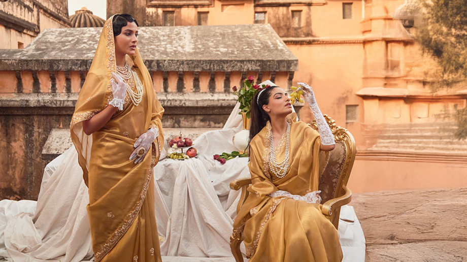 Two women wearing gold tissue sarees in a festive outdoor setting