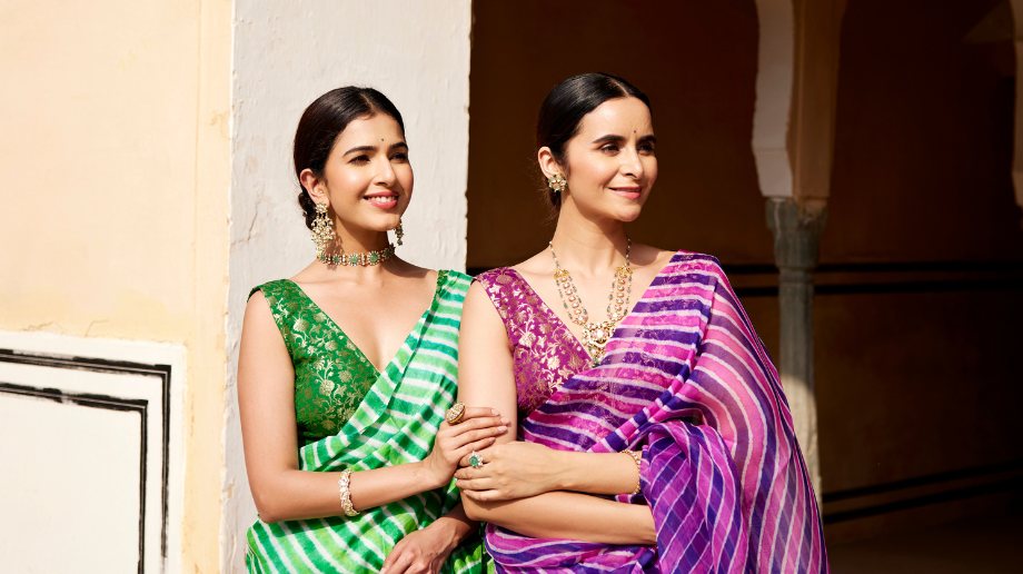 Two models wearing green and pink leheriya sarees in a heritage setting