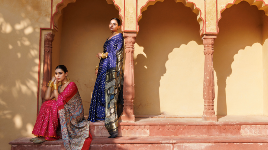 Two women wearing bandhani sarees posing in a heritage haveli with arches